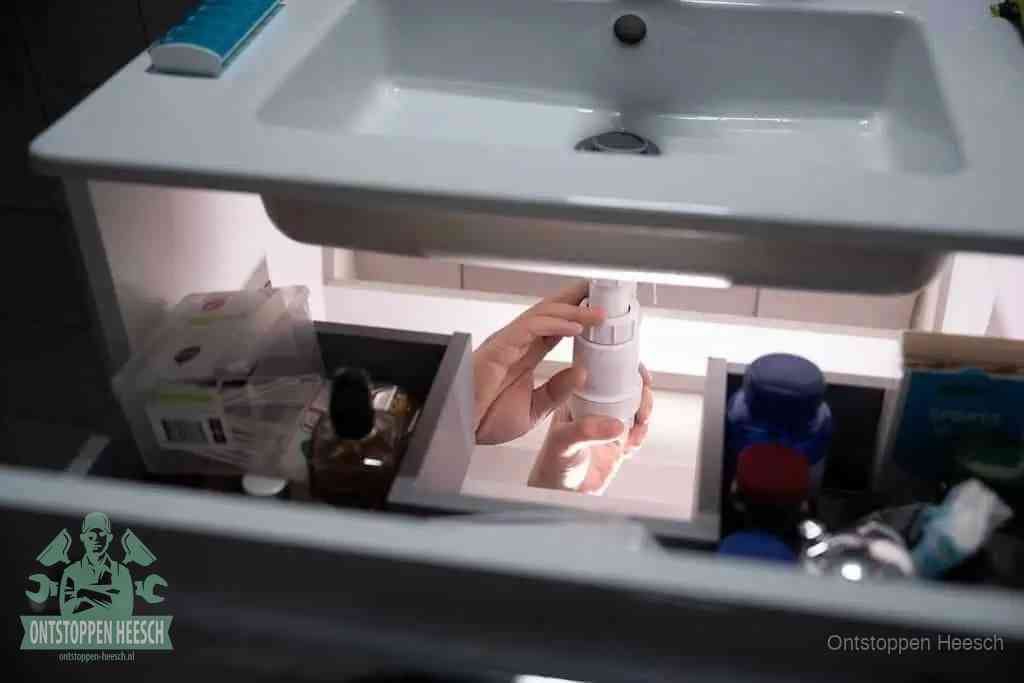 Een pompfles met zeep boven een wastafel, de heet water en afwasmiddel-methode om een vetprop in de afvoer los te maken in Heesch