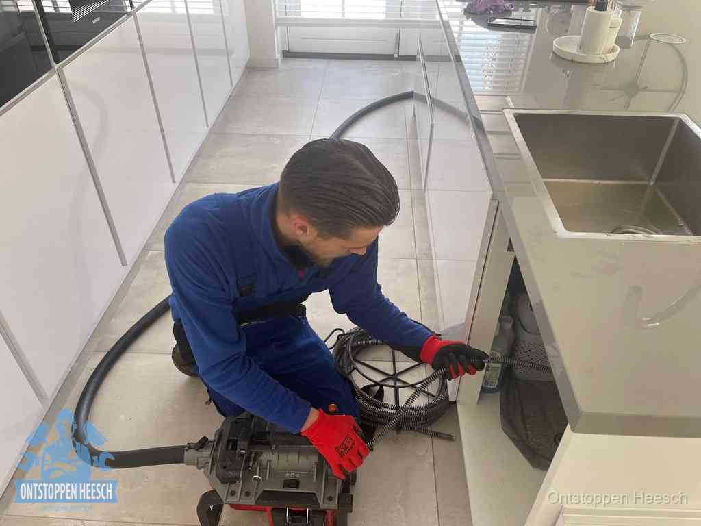 Een monteur ontstopt de keukenafvoer onder de spoelbak met een elektrische veermachine in Heesch