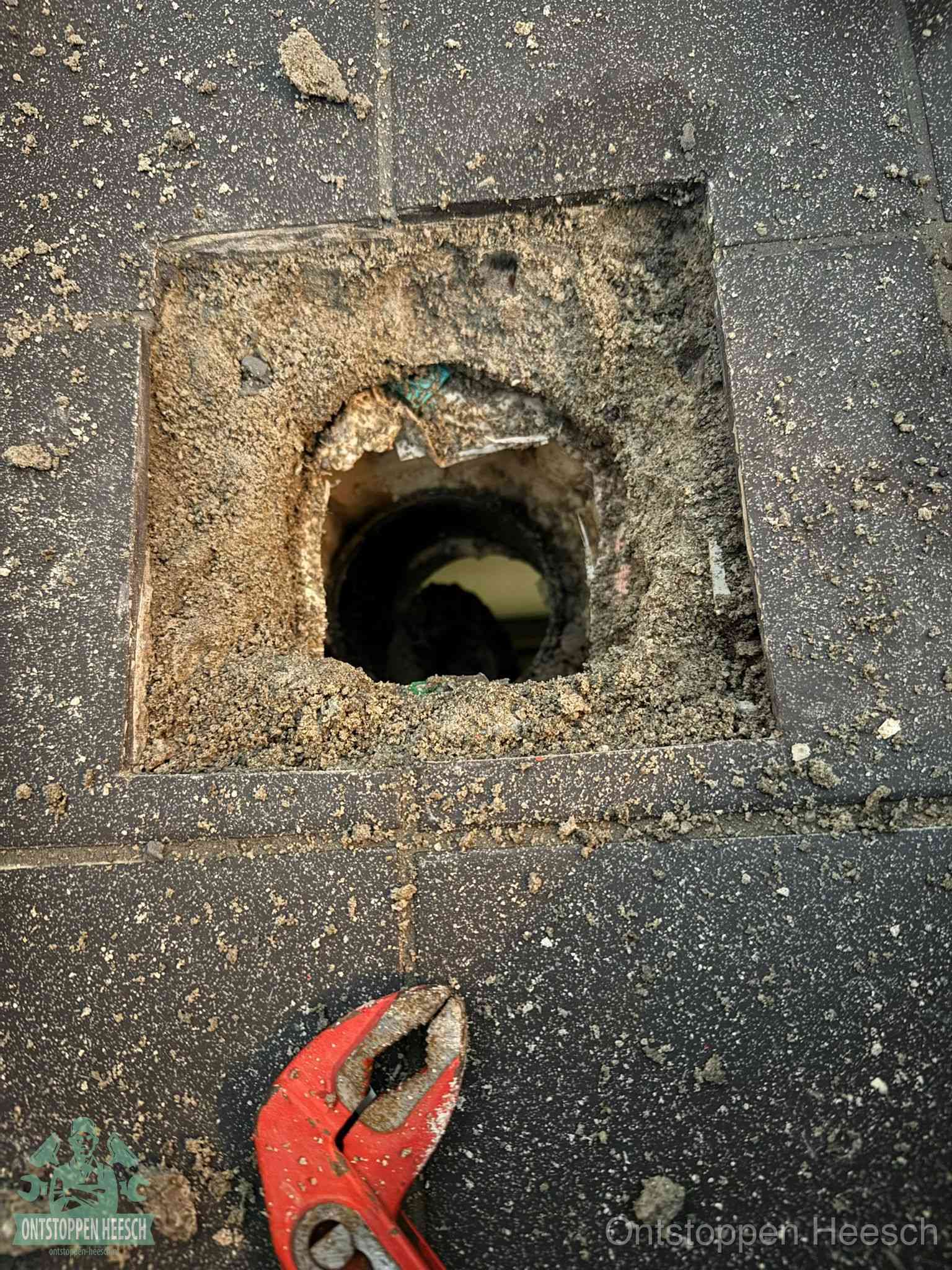 Een geopend rioolputje in een betontegelvloer met losgemaakt rooster en een zichtbare ronde afvoerbuis, het achterhalen waar de afvoerverstopping zit in Heesch