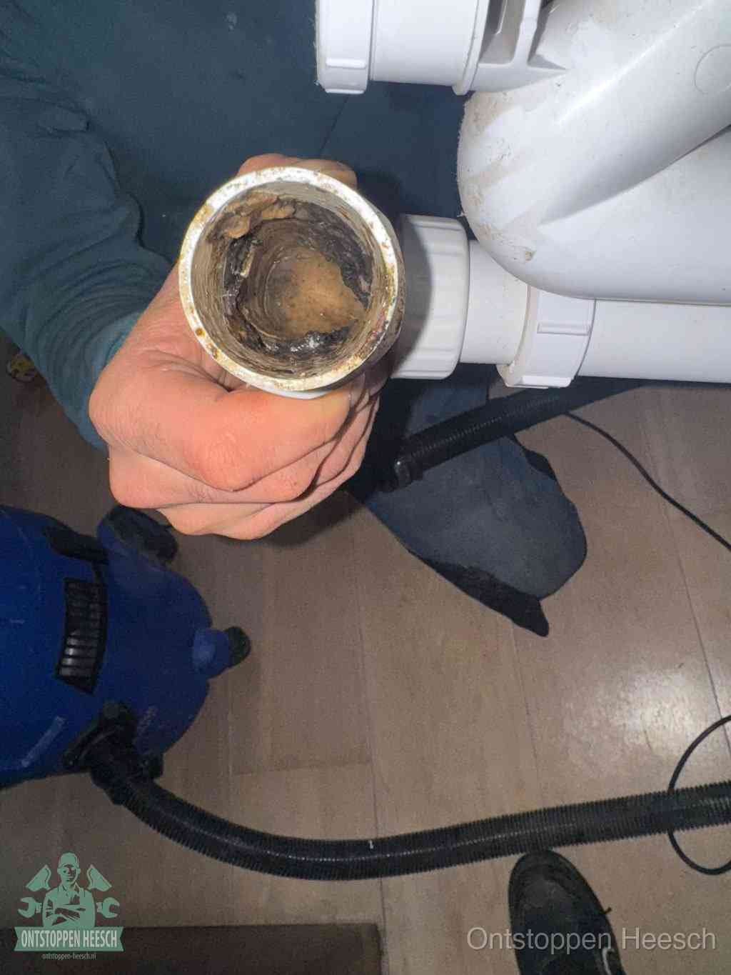 Een hand houdt een losgekoppeld PVC-afvoerbuisstuk vast dat van binnen volledig is dichtgeslibd met vet, vuil en aanslag, de meest voorkomende oorzaak van een verstopte afvoer in Heesch