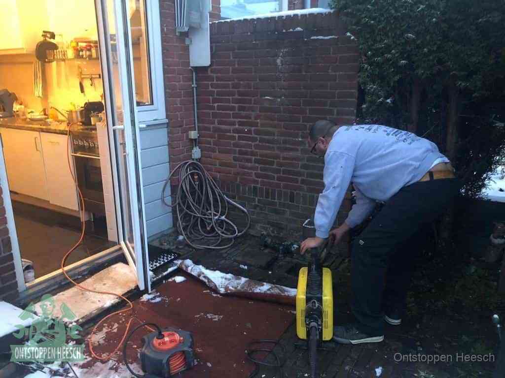 Een monteur werkt buiten bij een open riool-/grondput met een elektrische ontstoppingsmachine om een verborgen afvoerprobleem op te sporen in Heesch