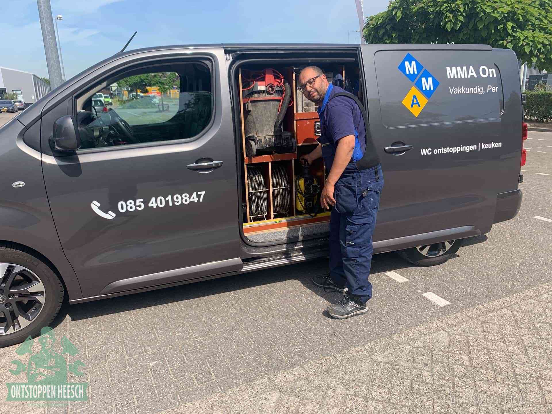 Een monteur bij de open schuifdeur van zijn bedrijfsbus op een parkeerplaats, klaar om de oorzaak van terugkerende afvoerverstoppingen aan te pakken in Heesch