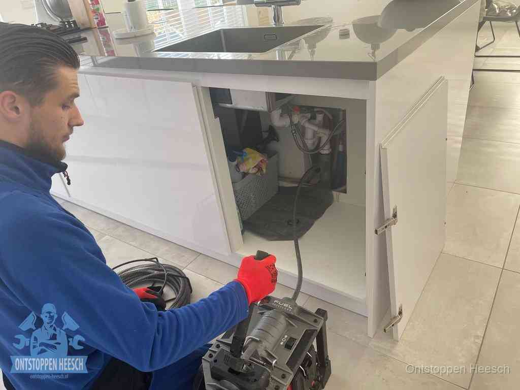 Monteur ontstopt met een veermachine een verstopte afvoer onder de gootsteen in Heesch