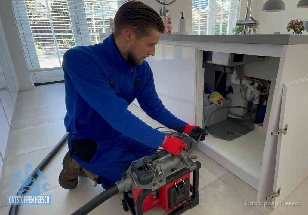 Een monteur voert een professionele elektrische ontstoppingsmachine in de afvoer onder de spoelbak tijdens het gootsteen ontstoppen in Heesch